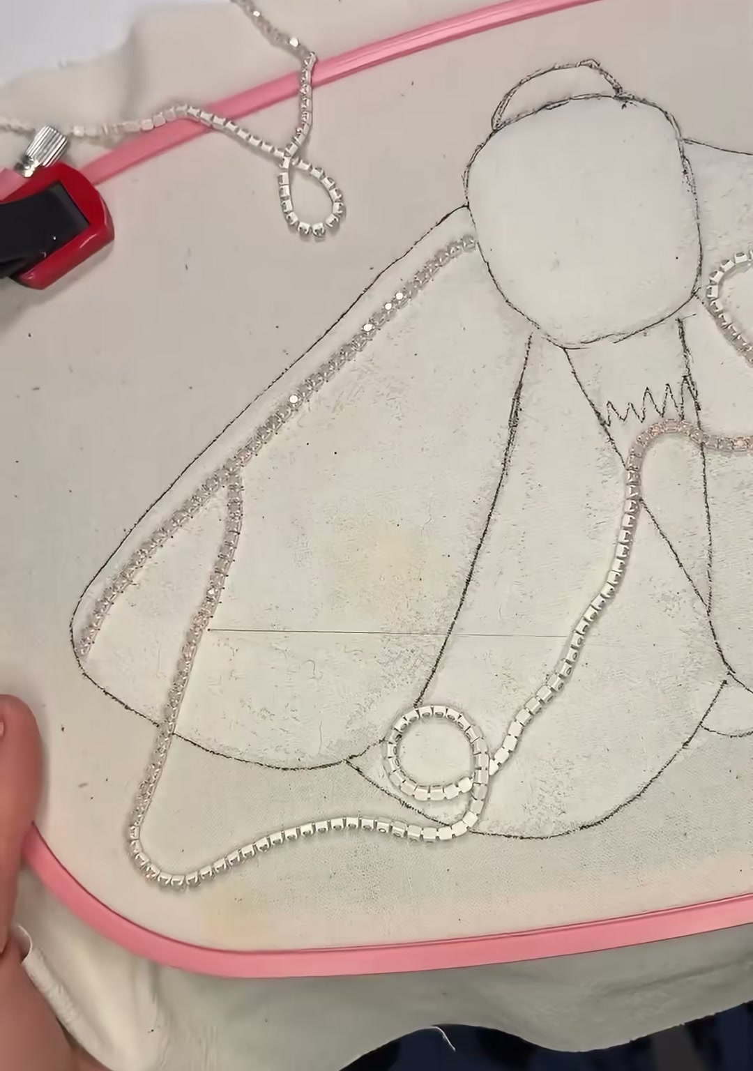 Step 02 — Silver cup-chain rhinestones following the drawn outline of the wings, creating a sparkling border on the fabric