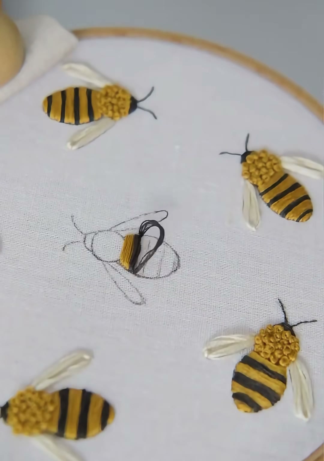 Step 01 — Several bee outlines drawn on fabric, with the first body partly stitched in yellow and black