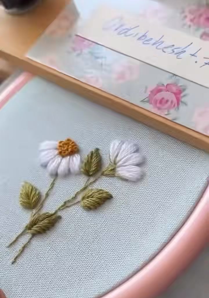 Close-up of the finished daisy embroidery with white petals, golden centers, and green leaves