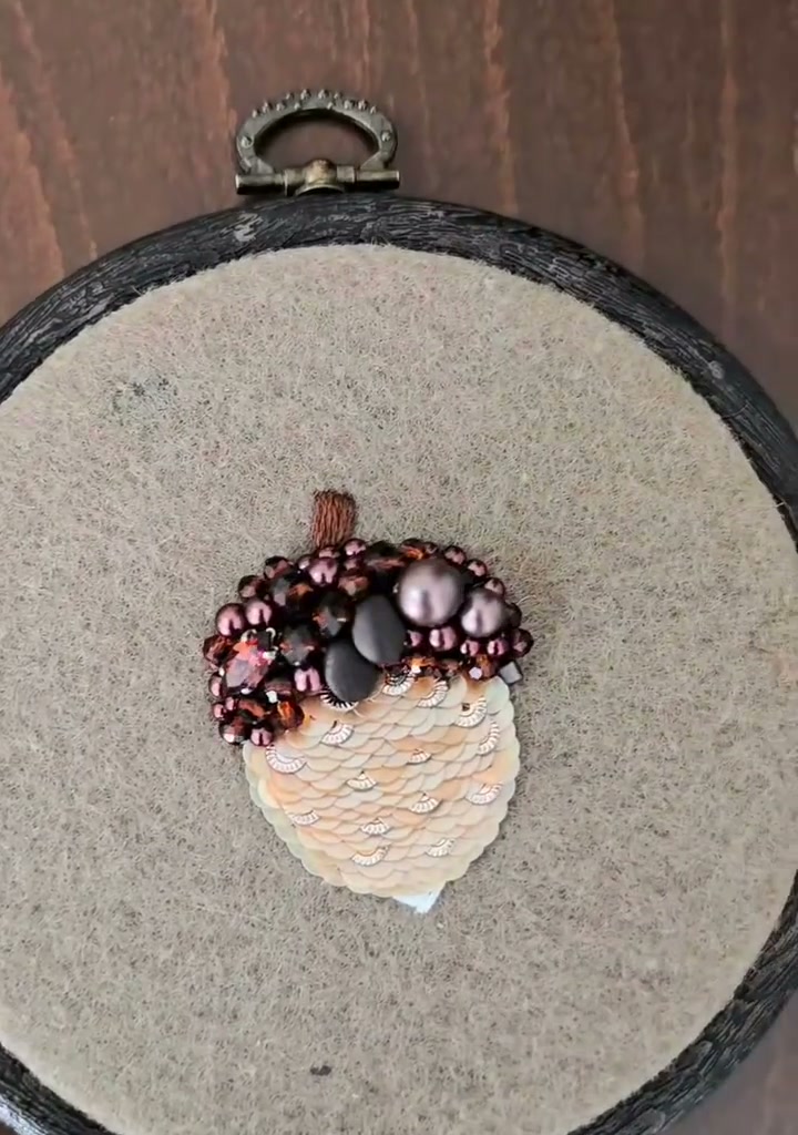 Step 18 — The completed acorn ornament hanging in its dark wooden hoop