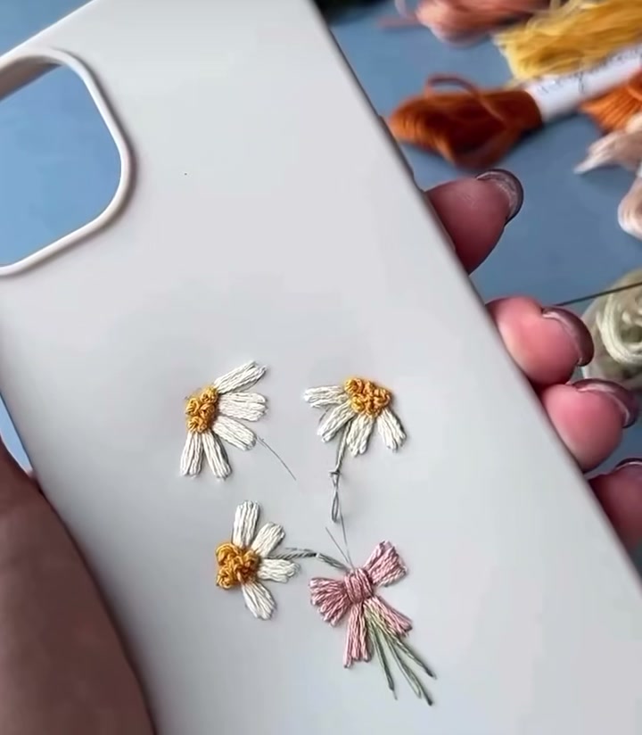 Step 10 — The completed embroidered daisy phone case held in hand